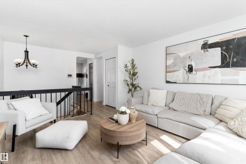 Bright interior with light wood-finish flooring, white walls, and a black metal stair railing - 15252 81 Street, Edmonton, AB 