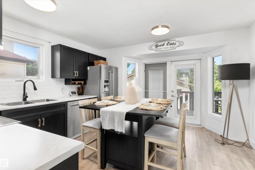 Bright kitchen featuring a bay window dining area, black cabinetry, white countertops, stainless steel appliances, and wood-finish flooring - 15252 81 Street, Edmonton, AB 