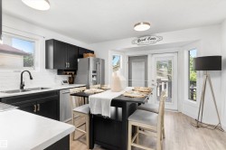 Bright kitchen featuring a bay window dining area, black cabinetry, white countertops, stainless steel appliances, and wood-finish flooring - 