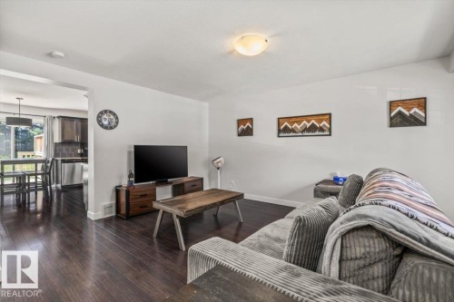 Spacious living area featuring dark wood-finish flooring, white walls, and a ceiling-mounted light fixture - 125 Birchwood Close, Devon, AB 