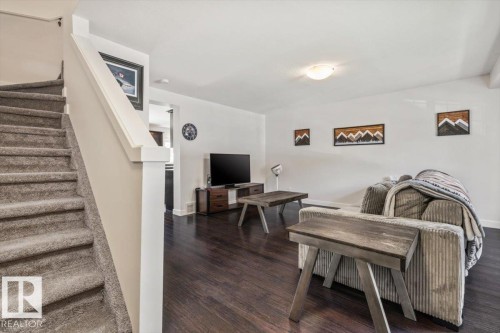 Staircase with carpeted treads and a white newel post, complementing the dark wood-finish flooring - 125 Birchwood Close, Devon, AB 