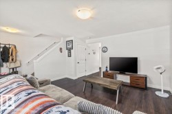 Spacious living area featuring dark wood-finish flooring, white walls, and a staircase with white risers and handrail - 