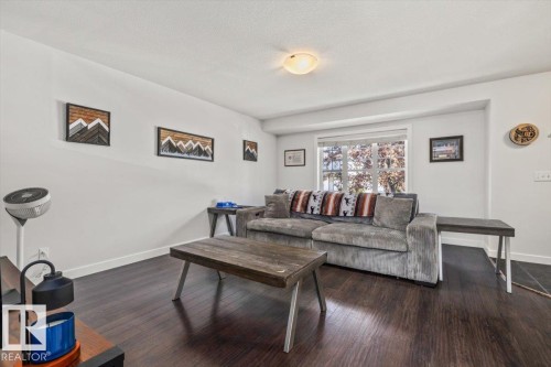 Spacious living area featuring dark wood-finish flooring, white baseboards, and a large window - 125 Birchwood Close, Devon, AB 
