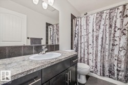 Bathroom featuring a light-colored countertop with an oval undermount sink, dark wood-finish cabinetry, a large mirror, and dark tile backsplash - 