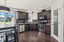 Kitchen featuring dark wood-finish cabinetry, stainless steel appliances, dark tile backsplash, and wood-finish flooring - 125 Birchwood Close, Devon, AB 