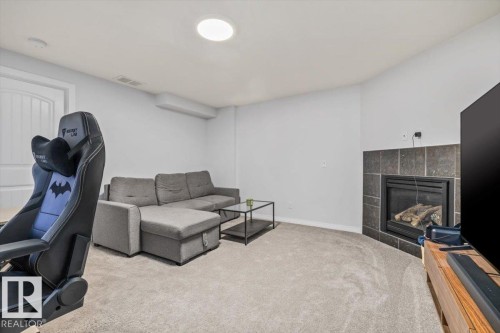 Carpeted living space featuring a fireplace with dark tile surround, a built-in circular ceiling light, and white trim - 125 Birchwood Close, Devon, AB 