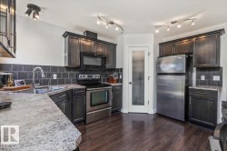 Kitchen featuring dark wood-finish cabinetry, stainless steel appliances, speckled countertops, a dark tile backsplash, and wood-finish flooring - 