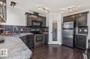 Kitchen featuring dark wood-finish cabinetry, stainless steel appliances, speckled countertops, a dark tile backsplash, and wood-finish flooring - 125 Birchwood Close, Devon, AB 