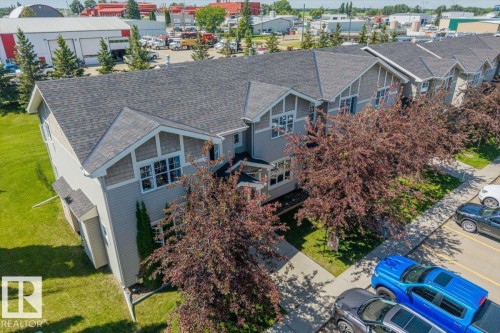 Modern townhome exterior featuring light gray siding, dark shingle roofing, and decorative gables with shingle accents - 125 Birchwood Close, Devon, AB 