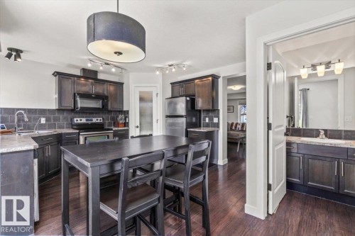 Kitchen featuring wood-finish flooring, dark cabinetry, stone countertops, and a tile backsplash - 125 Birchwood Close, Devon, AB 