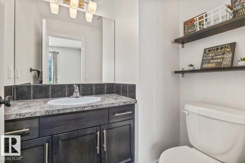 Bathroom featuring a dark wood-finish vanity with an integrated sink, granite-look countertop, and a dark tile backsplash - 125 Birchwood Close, Devon, AB 