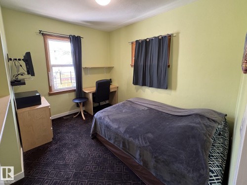 Bedroom featuring light green walls, a patterned dark carpet, and a window with a wood-finish frame - 11511 101 Street, Edmonton, AB 