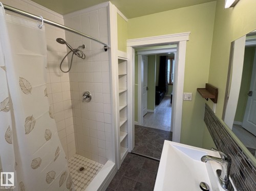 Bathroom featuring a white subway tile shower surround with a mosaic tile floor, built-in shelving, a vanity with a white rectangular sink, and a mirrored backsplash - 11511 101 Street, Edmonton, AB 