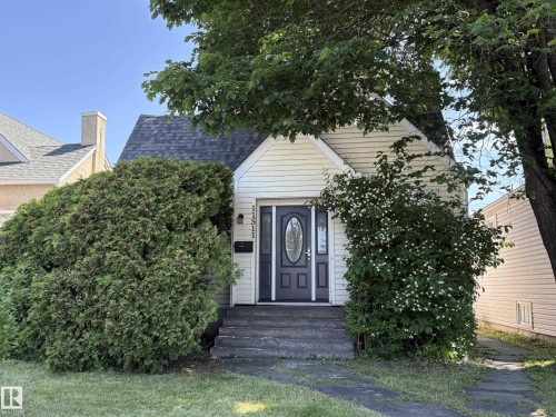 Charming cottage-style home featuring light-colored siding, a dark shingles roof, and an inviting front entrance with a dark door and clear glass insert - 11511 101 Street, Edmonton, AB 
