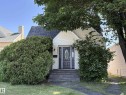 Charming cottage-style home featuring light-colored siding, a dark shingles roof, and an inviting front entrance with a dark door and clear glass insert - 11511 101 Street, Edmonton, AB 