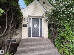 Cream-colored siding facade featuring a gray front door with an oval-shaped glass insert, concrete steps, and integrated address numbers - 