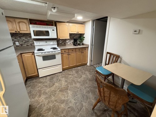 Kitchen area featuring wood-finish cabinetry, tile backsplash, and a white electric range with a built-in microwave - 11511 101 Street, Edmonton, AB 