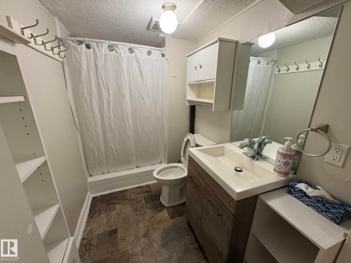 Bathroom featuring a single vanity with a rectangular sink, wood-finish cabinetry, and a large mirror - 11511 101 Street, Edmonton, AB 
