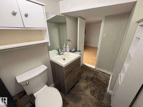 Bathroom featuring a vanity with a white basin and chrome faucet, a wall-mounted mirror, overhead cabinetry, and a toilet - 11511 101 Street, Edmonton, AB 