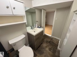 Bathroom featuring a vanity with a white basin and chrome faucet, a wall-mounted mirror, overhead cabinetry, and a toilet - 