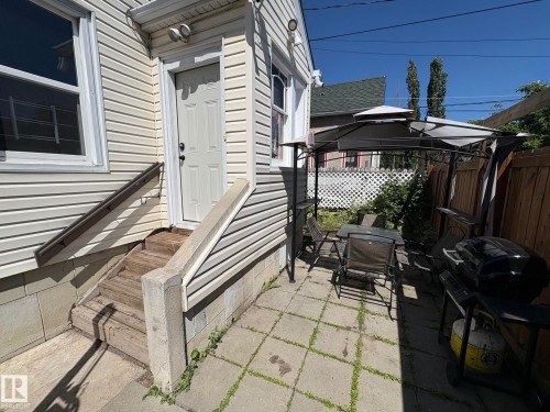 Exterior featuring horizontal vinyl siding, a white paneled door, and a concrete patio with pavers - 11511 101 Street, Edmonton, AB 