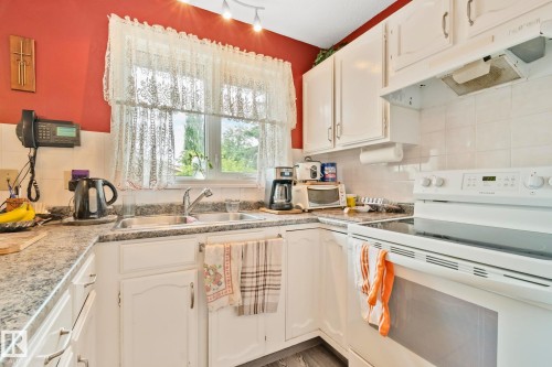 Kitchen featuring white cabinetry, stone-finish countertops, white tile backsplash, and a double basin stainless steel sink - 30 Garden Valley Drive, Stony Plain, AB - Indoor Photo Showing Kitchen With Double Sink