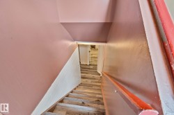 Staircase featuring wood-finish treads, a contrasting white and pink wall design, and a wooden handrail - 