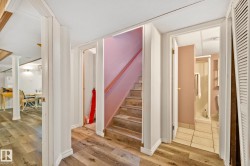 Lower-level hallway featuring wood-finish flooring, a staircase with a wooden handrail, and access to a bathroom with a shower stall and tiled flooring - 