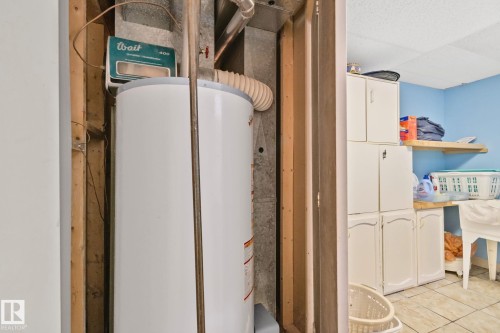 Utility area featuring a water heater, blue painted walls, white cabinetry, a wood shelf, and tiled flooring - 30 Garden Valley Drive, Stony Plain, AB - Indoor