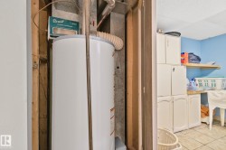 Utility area featuring a water heater, blue painted walls, white cabinetry, a wood shelf, and tiled flooring - 