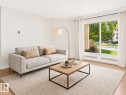 Bright living space featuring a large picture window, light wood-finish flooring, and white painted walls - 143 10636 120 Street, Edmonton, AB 