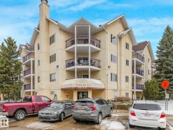Multi-story stucco exterior featuring multiple private balconies with purple railings, an arched entryway with an awning, and a peaked roofline - 