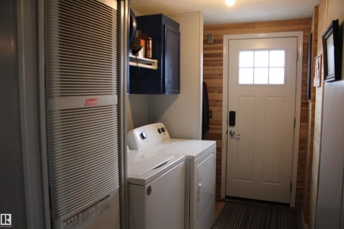 Entryway with wood-finish horizontal paneling, a white paneled door with a multi-pane window, and a built-in furnace with a vertical grate - 4839 49 Avenue, Chipman, AB 