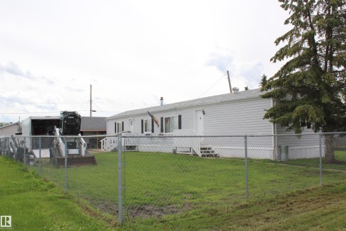 Exterior featuring white siding, a chain-link fence, and a mature evergreen tree - 4839 49 Avenue, Chipman, AB 