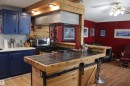 Kitchen featuring a tile-top island with a wood-finish base and barn door hardware, a built-in range, a stainless steel range hood, blue cabinetry, and wood-finish flooring - 4839 49 Avenue, Chipman, AB 