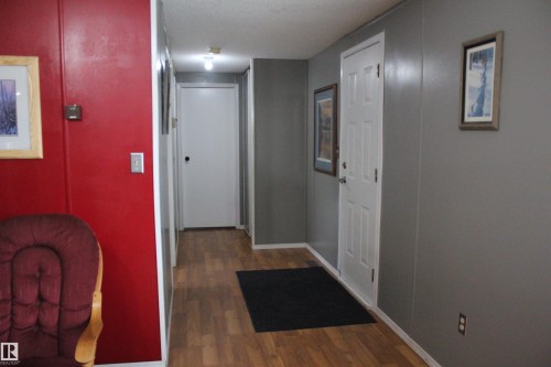 Hallway featuring wood-finish flooring, white trim, and a white paneled door - 4839 49 Avenue, Chipman, AB 