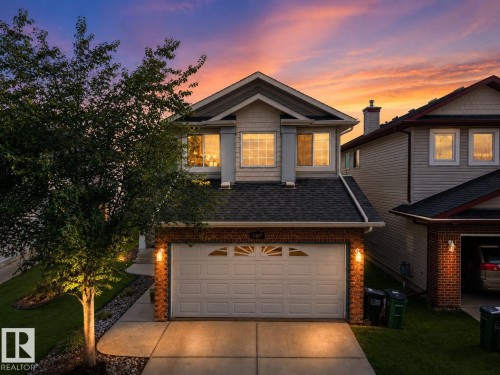 Two-story home featuring a brick facade with horizontal siding, an attached garage, a paved driveway, and mature landscaping - 7407 Singer Landing, Edmonton, AB 