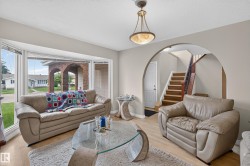 Bright living area featuring a large bay window with horizontal blinds, wood-finish flooring, and a ceiling-mounted light fixture - 