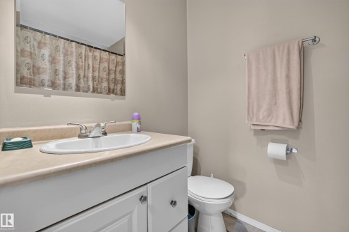 Bathroom featuring a vanity with a laminate countertop and integrated sink, a chrome two-handle faucet, white cabinetry with silver-tone hardware, and a toilet - 3841 62 Street, Edmonton, AB 