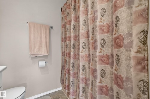 Bathroom featuring a patterned shower curtain, light-colored walls, and a white toilet - 3841 62 Street, Edmonton, AB 
