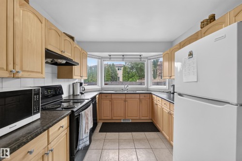 U-shaped kitchen featuring light wood cabinetry, dark countertops, and a bay window with a stainless steel sink - 3841 62 Street, Edmonton, AB 