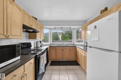 U-shaped kitchen featuring light wood cabinetry, dark countertops, and a bay window with a stainless steel sink - 