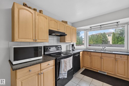 Kitchen featuring light wood-finish cabinetry, dark countertops, and a tile backsplash - 3841 62 Street, Edmonton, AB 