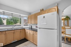 Kitchen featuring light wood cabinetry, dark countertops, a double basin sink, and a bay window - 
