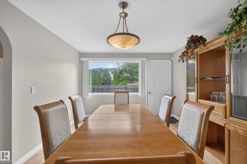 Dining area featuring wood-finish flooring, a contemporary pendant light fixture, a large window, a paneled door, and neutral wall tones - 3841 62 Street, Edmonton, AB 