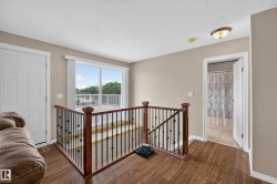 Upper-level landing featuring wood-finish flooring, a wood and wrought iron staircase railing, and a sliding glass door providing access to an exterior deck - 