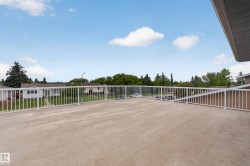 Expansive rooftop patio featuring a concrete surface, white metal railings, and an open-air setting - 