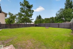 Spacious, fenced backyard featuring a manicured lawn, established privacy hedges, and a brick fire pit - 