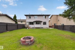 Expansive fenced backyard featuring a manicured lawn, a built-in fire pit, a ground-level deck, and a bay window - 