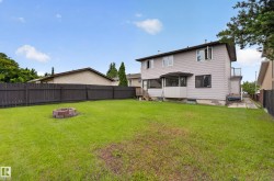 Expansive backyard featuring a manicured lawn, a brick-lined fire pit, and a dark-stained privacy fence - 